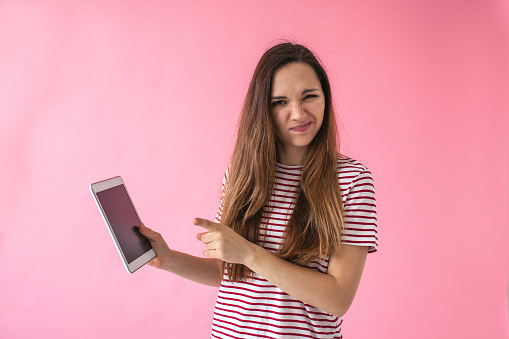 Dissatisfied girl uses tablet on a pink background. Bad news or another reason.