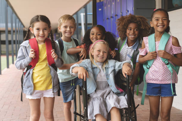 miúdos felizes da escola que estão no corredor quando estudante que senta-se na cadeira de rodas - criança de escola fotos - fotografias e filmes do acervo