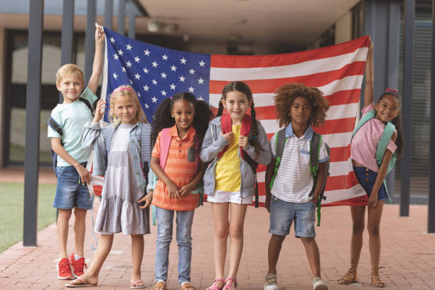 studenti della scuola felice in piedi nel corridoio mentre tengono la bandiera americana - youth culture foto e immagini stock