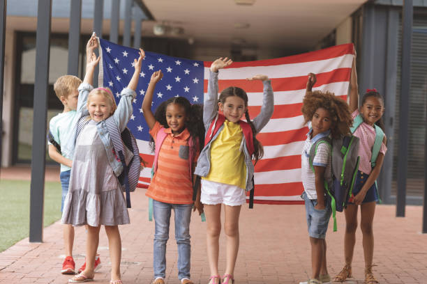 istock Happy school students standing in corridor while holding american flag 1138363052