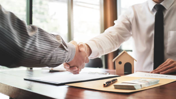 Real estate agent shaking hands with customer with house model and contract paper. stock photo