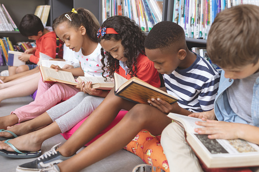 Los niños de la escuela sentados en cojines y estudiando sobre libros en una biblioteca photo