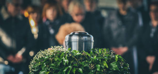 Metal urn at a funeral A metal urn with ashes of a dead person on a funeral, with people mourning in the background on a memorial service. Sad grieving moment at the end of a life. Last farewell to a person in an urn. decorative urn stock pictures, royalty-free photos & images