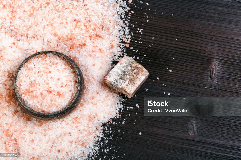 top view of salt cellar and pink Salt on table top view of silver salt cellar, rough natural pink Halite mineral and grained Himalayan Salt on dark brown wooden board Salt - Mineral Stock Photo