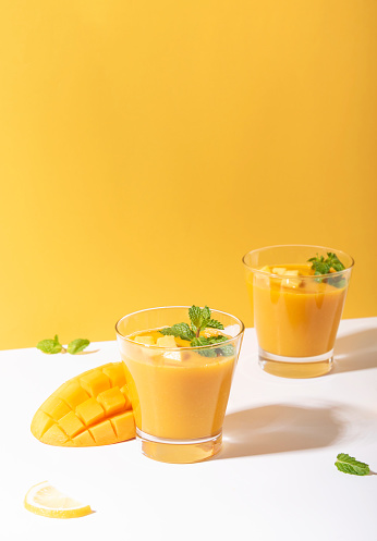 Fresh mango smoothie and ripe mango slice on yellow background. summer drink.