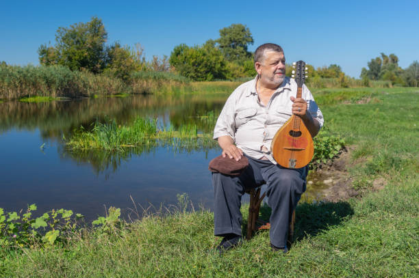 istock Man having rest on a riverside sitting on a wicker stool with mandolin 1138371460