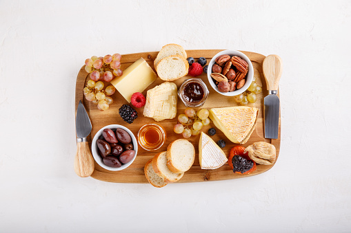 Cheese plate. French cheese with nuts, grape, berries, dried fruits and honey on cutting board on white. Camembert, Livarote, Pont-L'eveque cheese from Normandy and comte cheese. Top view.