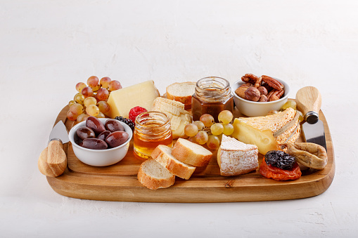 Cheese plate. French cheese with nuts, grape, berries, dried fruits and honey on cutting board on white. Camembert, Livarote, Pont-L'eveque cheese from Normandy and comte cheese.