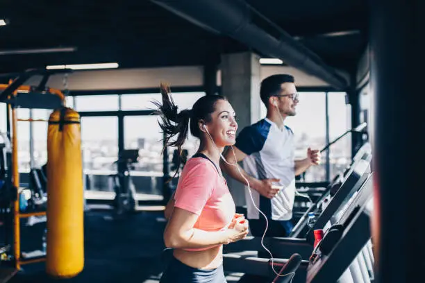 Young fit man and woman running on treadmill in modern fitness gym.