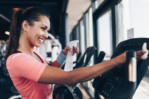 Woman cleaning fitness gym equipment Young happy and smiling woman cleaning and weeping expensive fitness gym equipment with sprayer and cloth. gymcleaning stock pictures, royalty-free photos & images