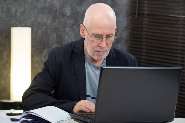 istock senior man with a beard and blue shirt in the office using laptop 1138377035