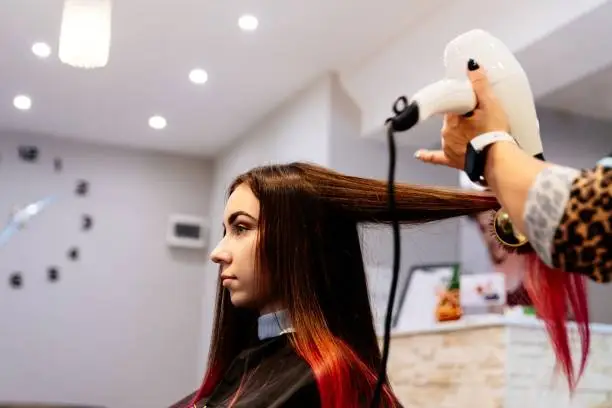 Hairdresser drying woman hair with hairdryer. Female in hairdresser salon