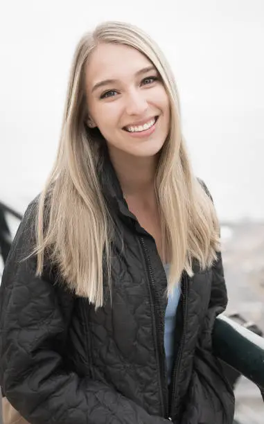 Beautiful young woman with long strait blonde hair and blue eyes on a foggy background in the city.