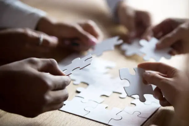 Photo of Close up members of multiracial team assembling white puzzle