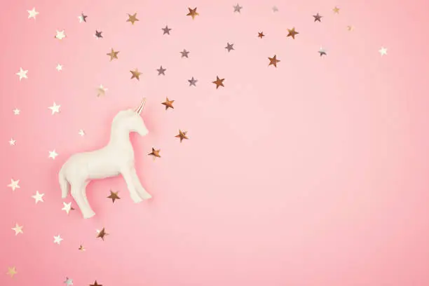 Flat lay with white unicorn and stars over the pink background