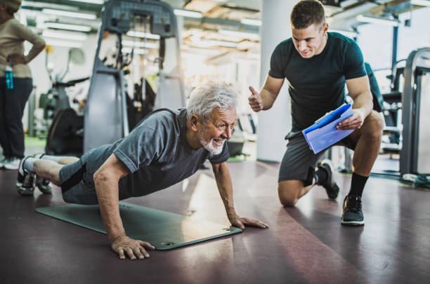 Come on, one more push-up! Happy senior man exercising push-ups in a gym while young coach is counting him. fitness instructor stock pictures, royalty-free photos & images