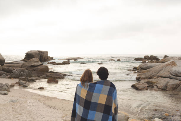 istock Caucasian couple wrapped in blanket standing at  beach 1138386460