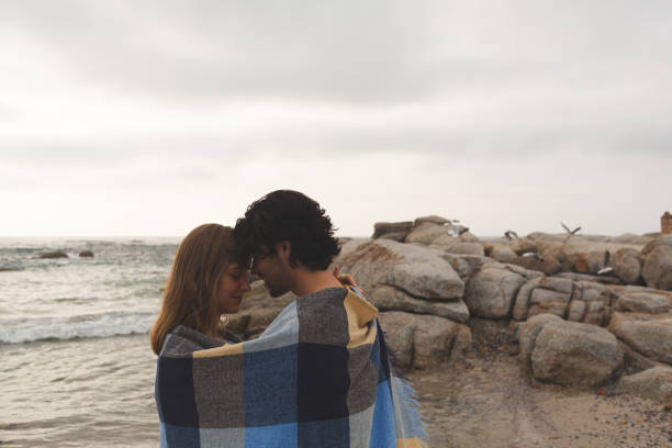 istock Caucasian couple wrapped in blanket standing at beach 1138386493