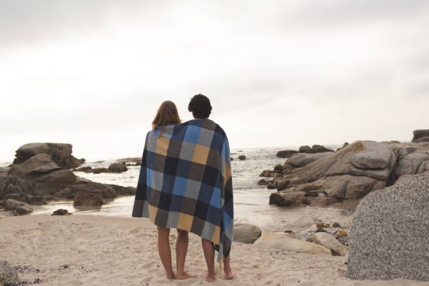 istock Caucasian couple wrapped in blanket standing at beach 1138386498