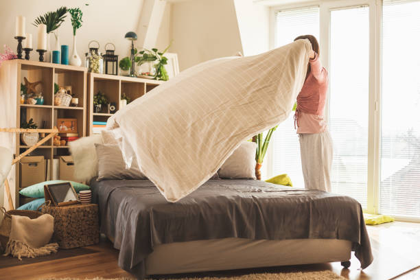 donna che diffonde una trapunta su un letto matrimoniale a casa - home interior sparse bedroom inside of foto e immagini stock