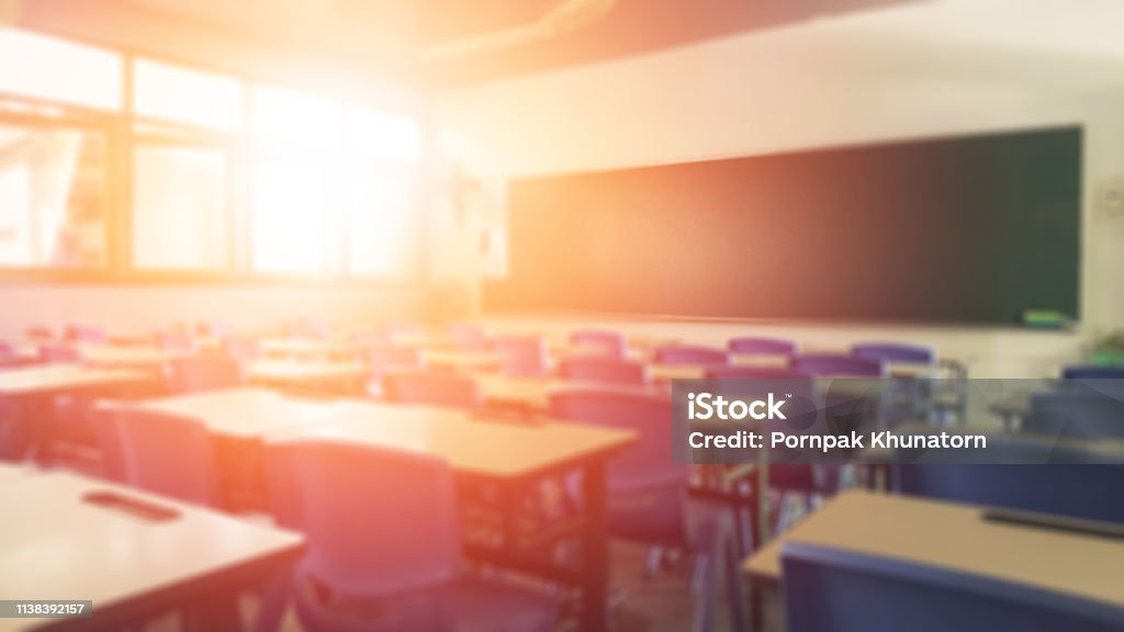 School classroom in blur background without young student; Blurry view of elementary class room no kid or teacher with chairs and tables in campus. Education Stock Photo