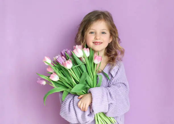 Photo of Beautiful girl holding a bouquet of tulip flowers on a light background.