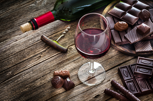 High angle view of a red wineglass and a selection of various chocolate bars, truffles and pralines shot on rustic wooden table. A wine bottle is at background and complete the composition. Copy space available for text and/or logo. Predominant color is brown. Low key DSRL studio photo taken with Canon EOS 5D Mk II and Canon EF 100mm f/2.8L Macro IS USM.