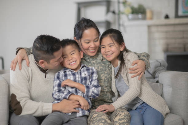 Military Family Sitting On Couch A family of four is happily sitting on the sofa in their living room. The mother has just returned home from serving her country and is wearing a military uniform. filipino family stock pictures, royalty-free photos & images