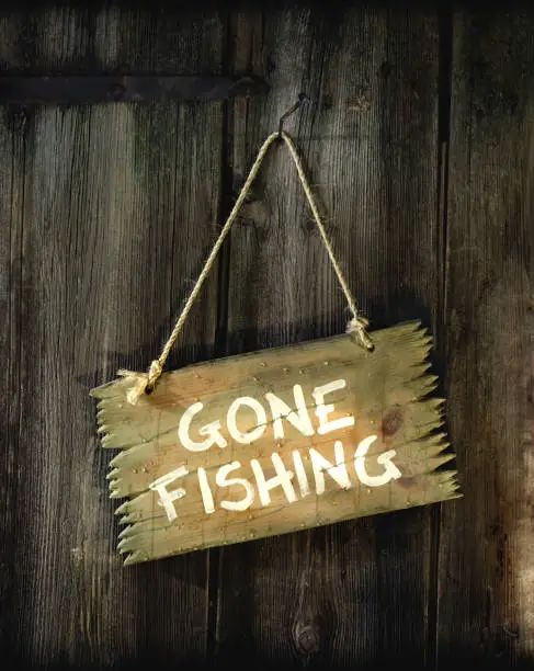 Sign "Gone fishing" hangs on the door made of old wood."u2028