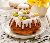 Easter yeast cake (Babka) covered with icing and decorated with marzipan eggs on a white plate on a wooden table.