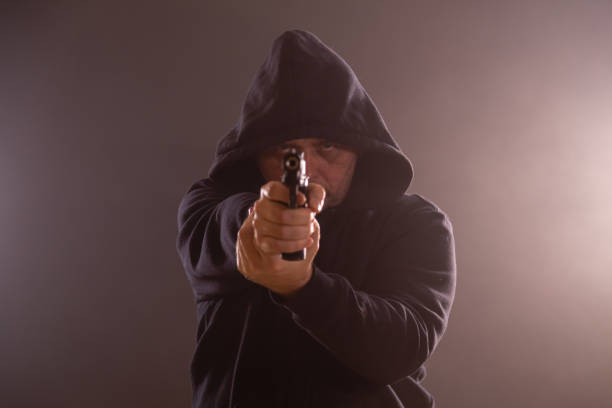 istock Man in black hoodie points pistol 1138403769
