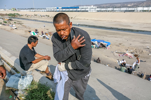 Tijuana, Mexico, Nov 10 - A Central American and Mexican migrant lives in a Tijuana canal near the iron and steel wall that borders and protects the US-Mexican border, waiting to cross the border. Behind, on the top of the canal, is the boundary wall line.