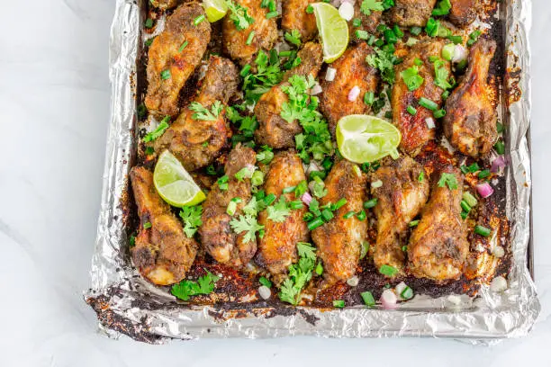 Vibrant and Colorful Photo of Jamaican Style Jerk Chicken Wings with Lots of Greens on Top in a Baking Sheet. Full Frame Photo of Chicken Wings.