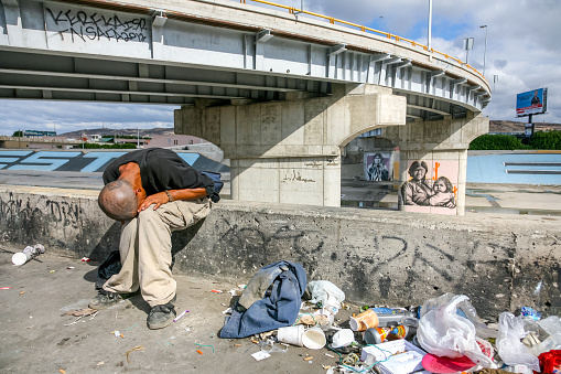 Tijuana, Mexico, Nov 10 - A migrant lives in extreme poverty in a Tijuana canal near the iron and steel wall that separates and protects the US-Mexican border. In the background, to the left, runs the boundary line and the border station of San Ysidro.