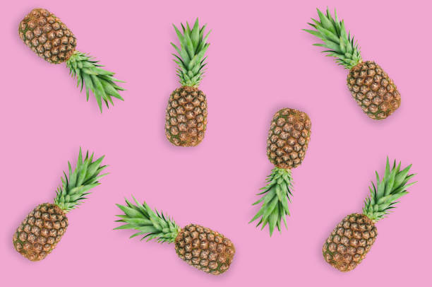 istock Scattered fresh whole pineapples with green leaves lying on pink table on kitchen. Top view. Cooking concept 1138417637