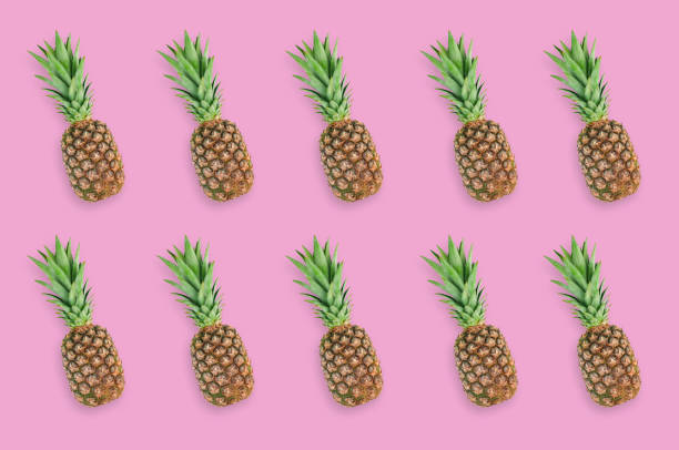 istock Rows of fresh whole pineapples with green leaves lying on pink table on kitchen. Top view. Cooking concept 1138417651
