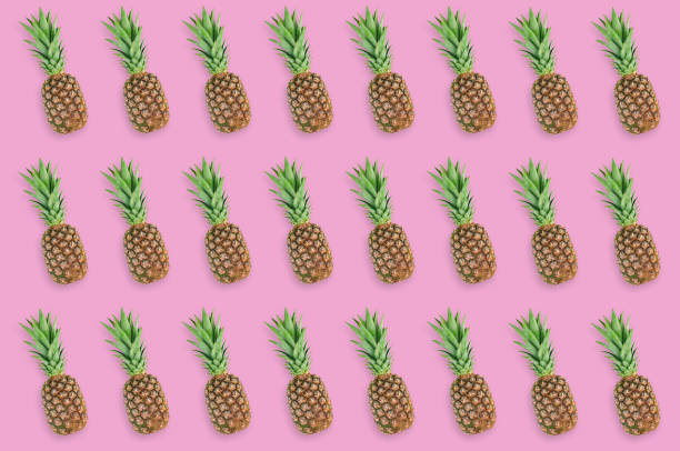 istock Horizontal rows of fresh whole pineapples with green leaves lying on pink table on kitchen. Top view. Cooking concept. Seamless pattern 1138417652