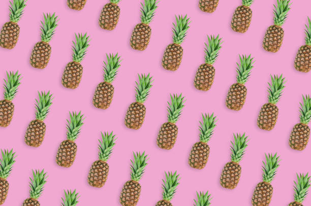 istock Diagonal rows of fresh whole pineapples with green leaves lying on pink table on kitchen. Top view. Cooking concept 1138417662