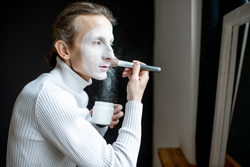 Actor putting mime makeup on his face preparing for perfomence indoors
