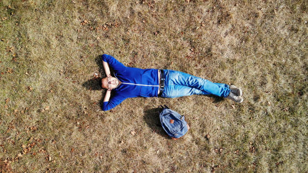 Young caucasian man lying in grass, relaxing. Shot with drone directly above, aerial view.