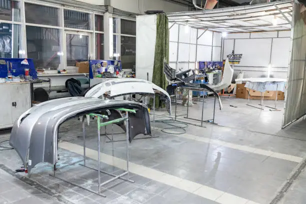 Three auto bumpers  parts are installed on the racks after painting in the car repair shop in the room with tools and equipment for repairing body parts after an accident