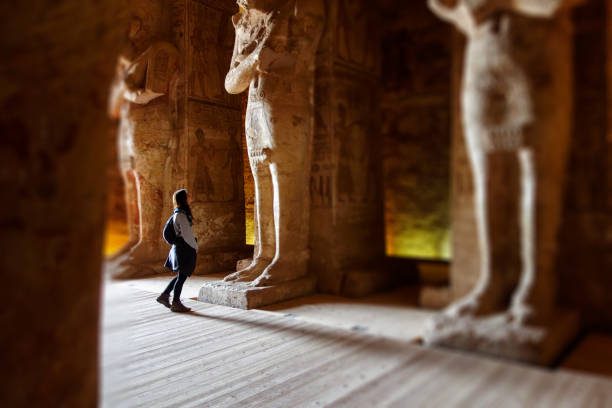 Young millennial Traveller tourist inside Rameses II Temple in Abu Simbel between gigantic statues seems small stock photo