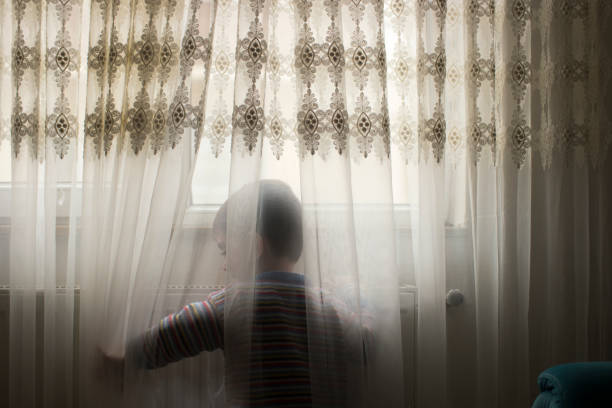 istock Shy cute little boy behind curtains 1138431300