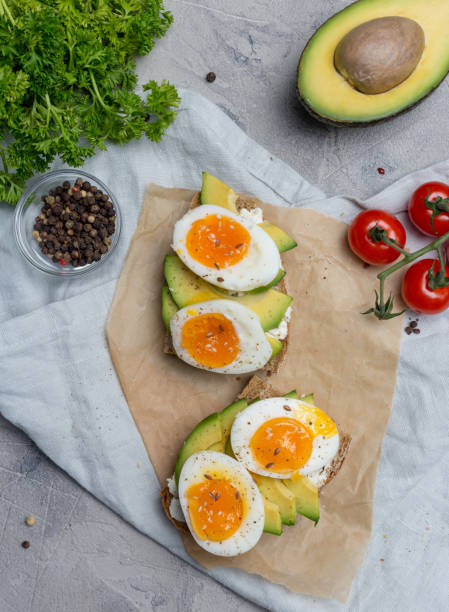 Sandwich on grain bread with boiled egg and avocado Sandwich on grain bread with boiled egg and avocado on craft paper, parsley, cherry tomatoes, napkin near on gray background. Concept of healthy food. Holiday Easter breakfast egg cherry tomato rye stock pictures, royalty-free photos & images