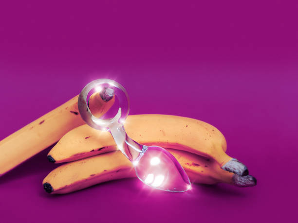 Glass sex toy and a yellow banana are on a colored background stock photo