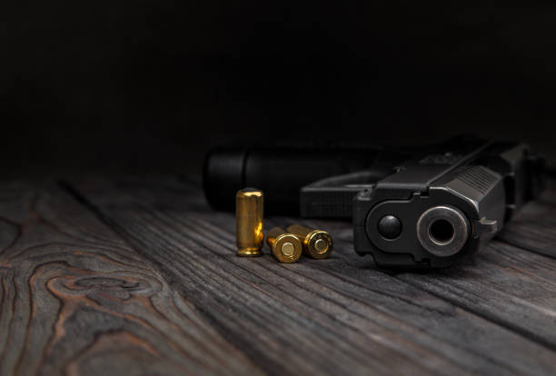 black pistol and cartridges on a brown wooden background black pistol and cartridges on a brown wooden background gun mafia handgun bullet stock pictures, royalty-free photos & images