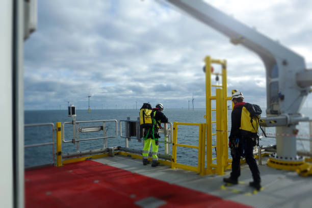 Offshore manual worker standing on deck with wind-turbines behind them stock photo
