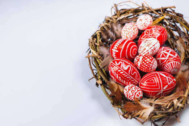 istock Easter red eggs with folk white pattern inside bird nest on white background. Top view. 1138449316