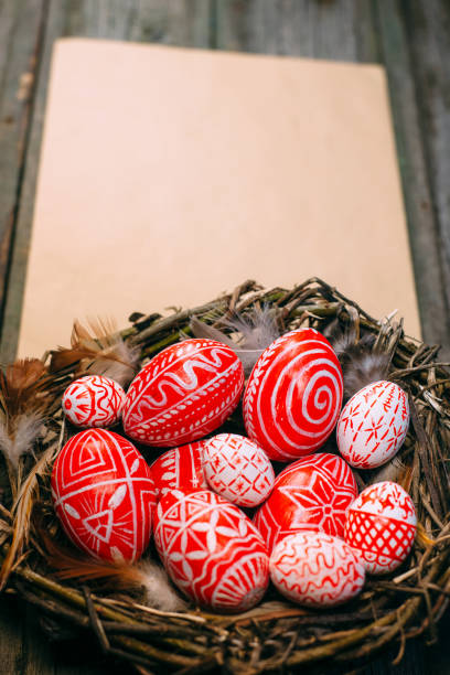 istock Easter red eggs with folk white pattern inside bird nest on sheet of paper on rustic wood background. 1138449397