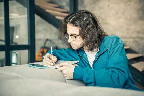 Photo of Attentive long-haired guy with long hair rewriting notes in album
